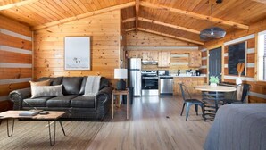 A cozy cabin interior with a living area featuring a sofa and coffee table, a kitchen with modern appliances, and a dining area with chairs.
