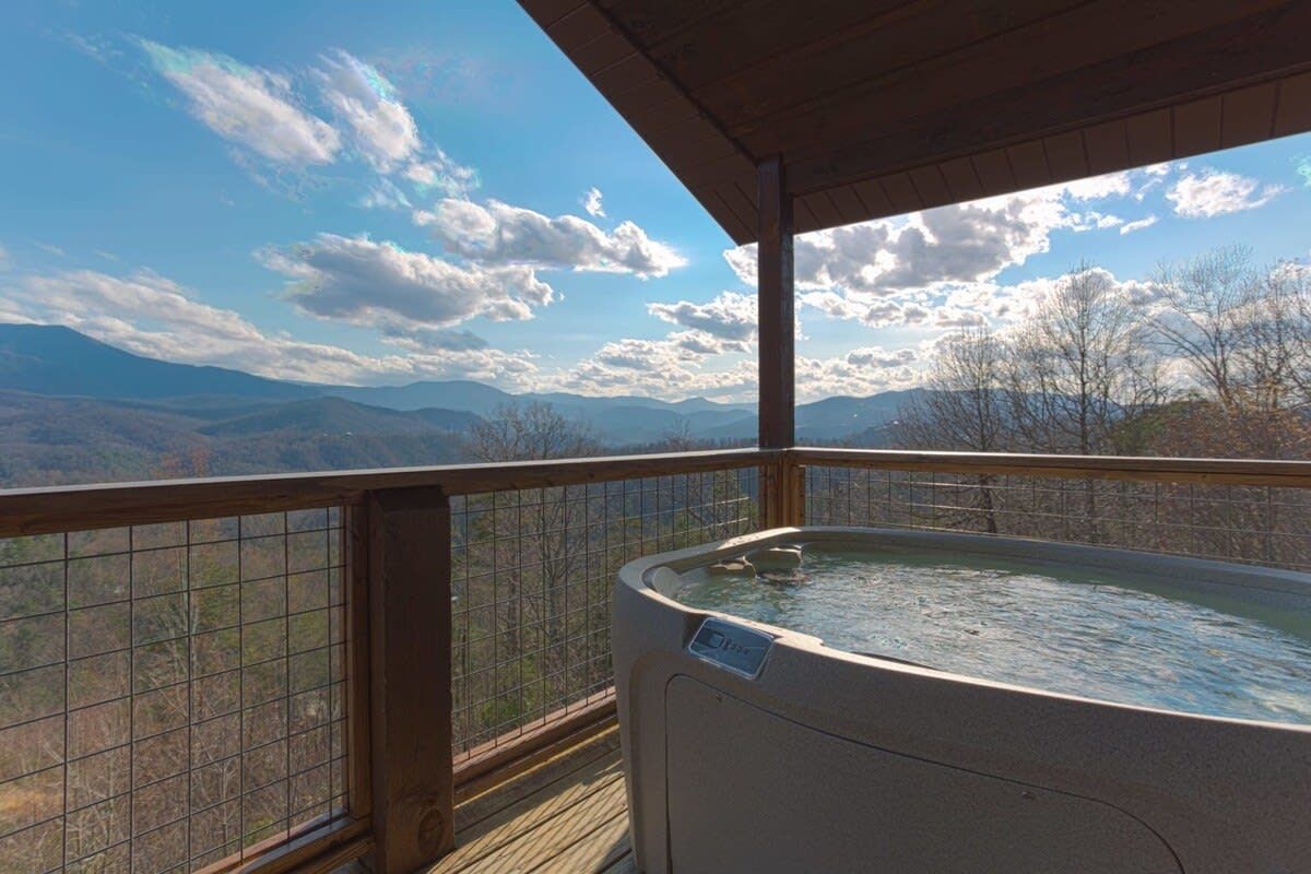 A hot tub on a wooden deck with a view of mountains and trees.