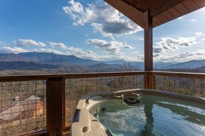 A hot tub with a view of mountains and a fenced balcony.