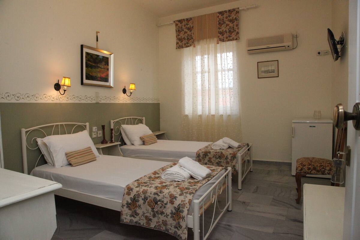 A hotel room with two beds, a small desk, a chair, and a refrigerator.
