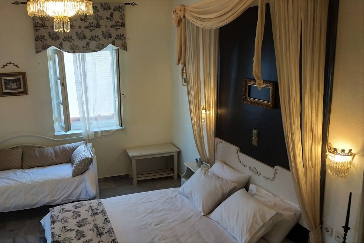 A bedroom with two beds, a window with sheer curtains, a chandelier, and a wall-mounted picture frame.