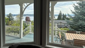 Een kamer met een groot raam dat uitzicht biedt op een balkon, een houten terras en een verafgelegen waterpartij.