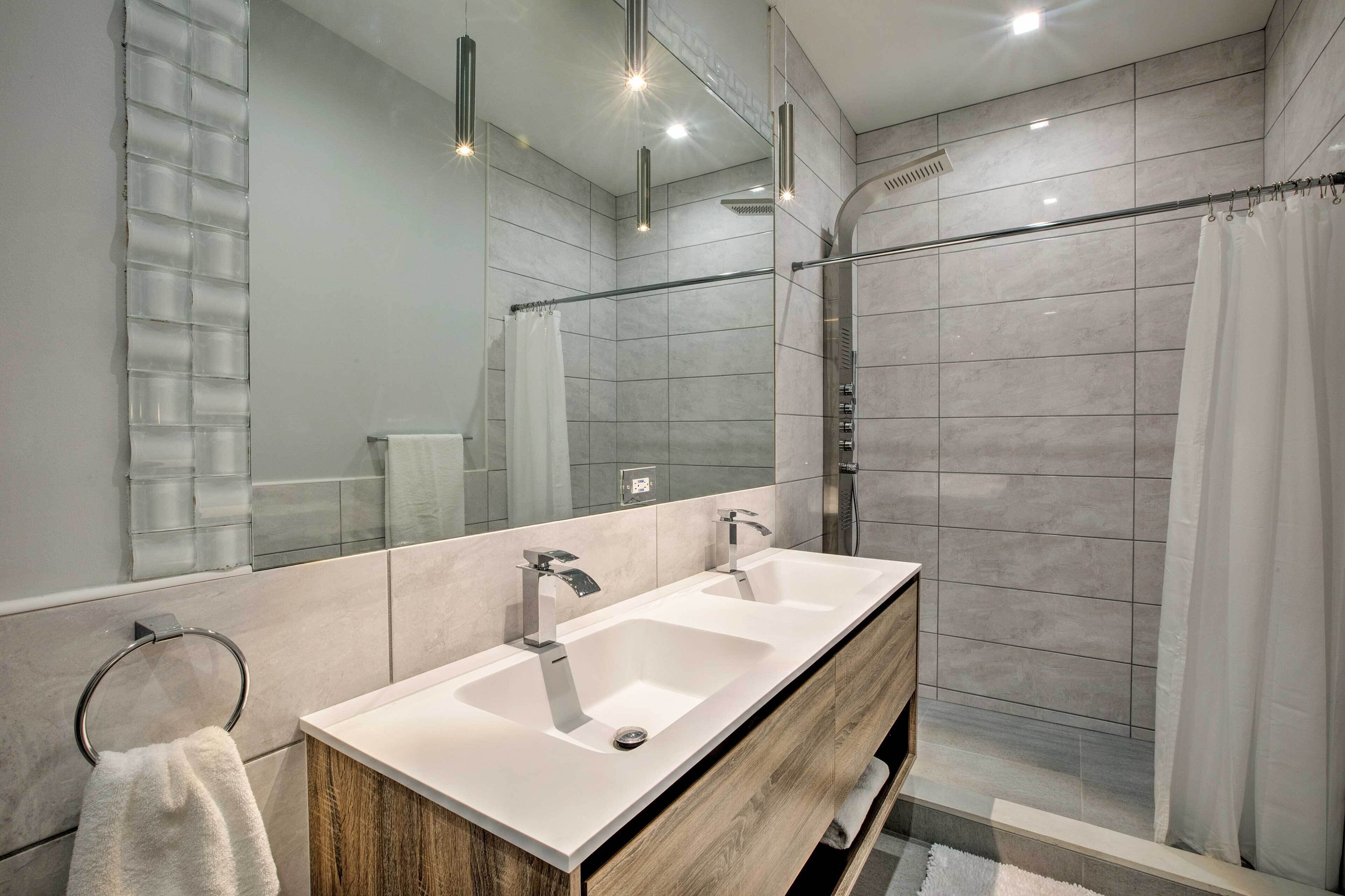 Een moderne badkamer met twee wasbakken, een douche en een grote spiegel.