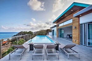 Zona de piscina exterior moderna amb gandules, vista a l'oceà i un edifici contemporani amb grans finestres.