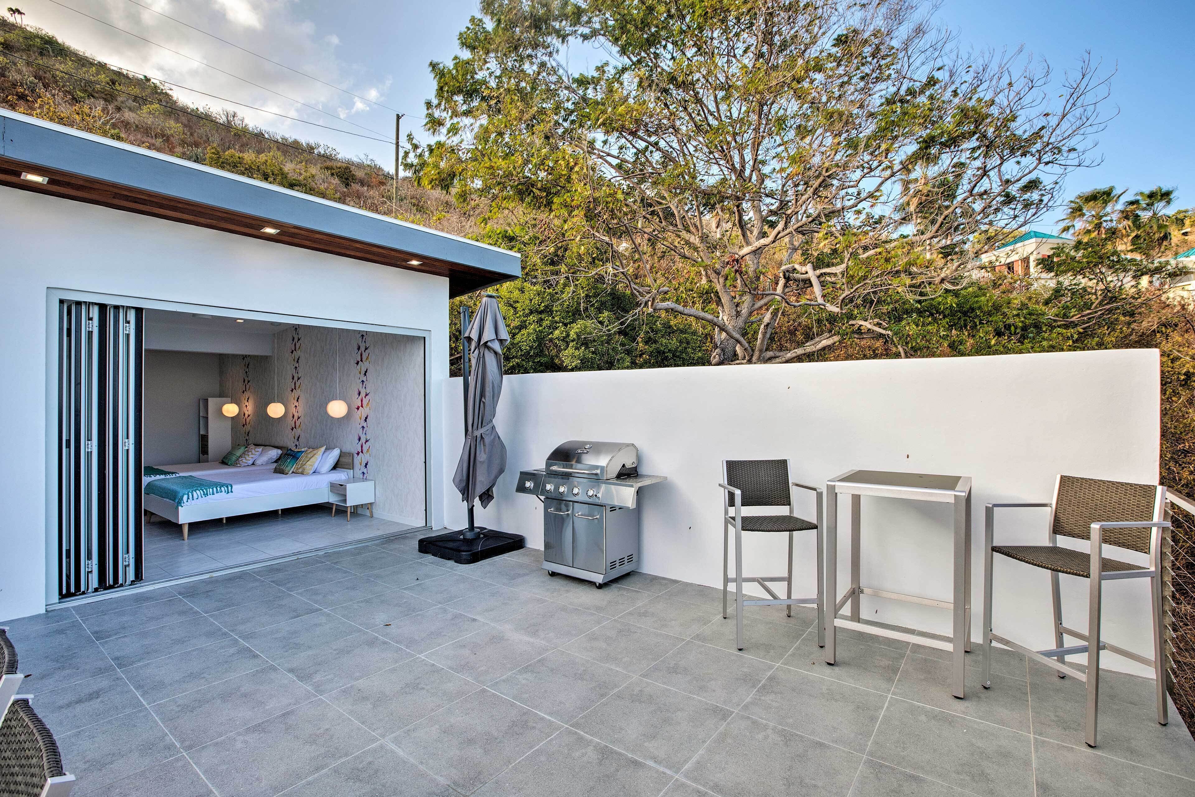 A modern outdoor patio with a grill, seating area, and a bedroom with a sliding door.