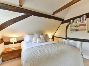 A bedroom with a sloped ceiling, a bed with white bedding, a nightstand with a lamp, and a bookshelf with books. - 2 bedroom accommodation in Cheriton (Cheriton)