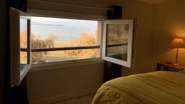 A bedroom with a bed, a window with a view of the sea, and a bedside lamp.