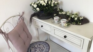 A white metal chair with a cushion, a small round table with a patterned tray, and a white dresser with two floral cups and a potted plant. - Refined detached villa for nature lovers. (Domus De Maria)