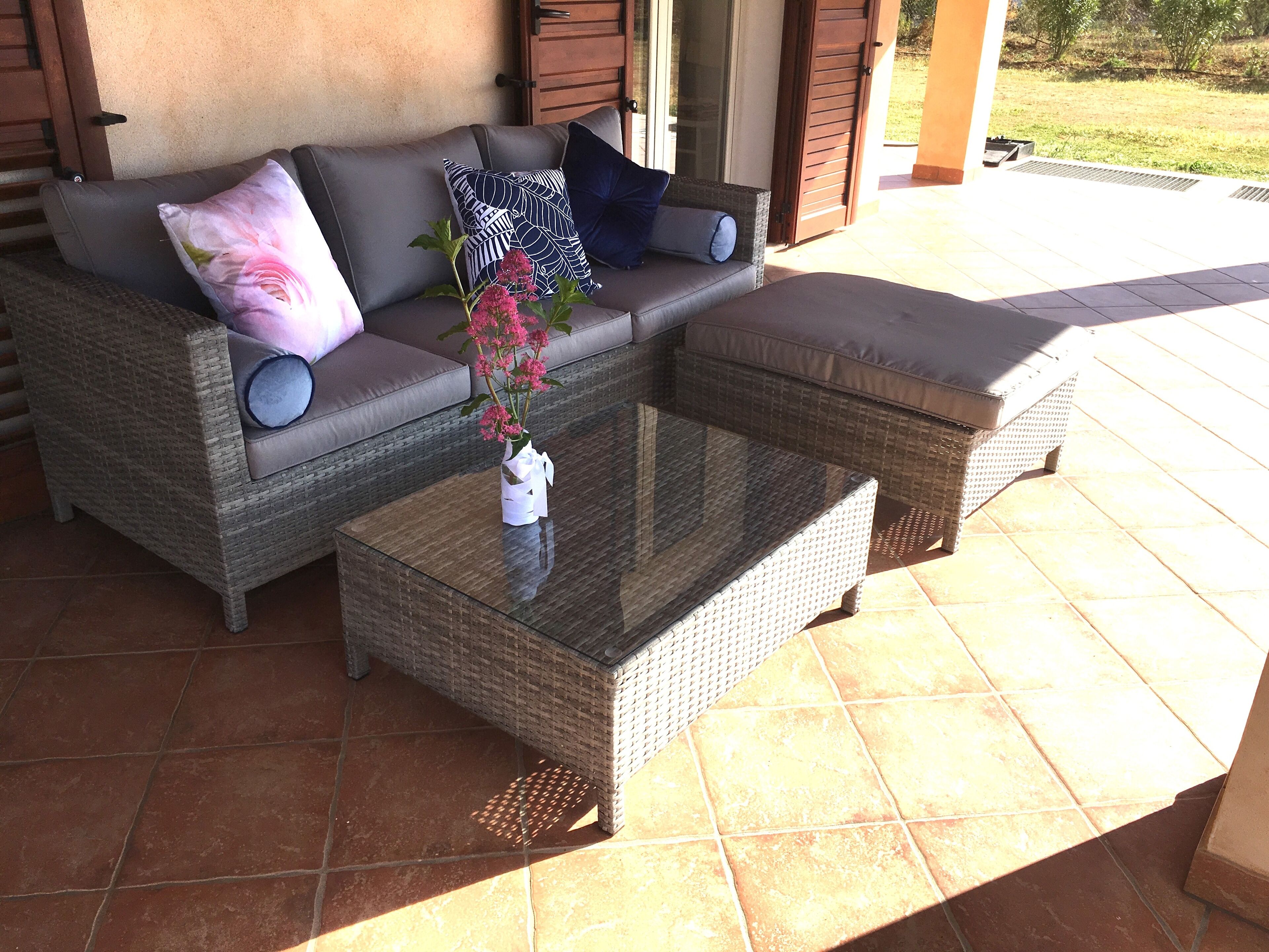 A wicker sofa with cushions and a glass coffee table with a vase of flowers.