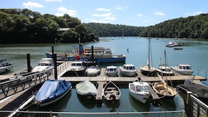 Un port de plaisance où sont amarrés différents types de bateaux, le tout bordé de quais en bois et entouré d’une colline boisée.
