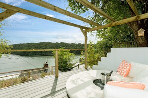 A wooden deck with a white sofa and orange pillows, overlooking a river and forested hills. - Fal River Cottage - sleeps 3 guests  in 2 bedrooms (Truro)