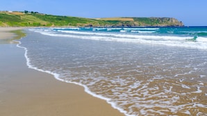 Une plage avec une eau d’un bleu limpide, un rivage sablonneux et des collines verdoyantes en arrière-plan.