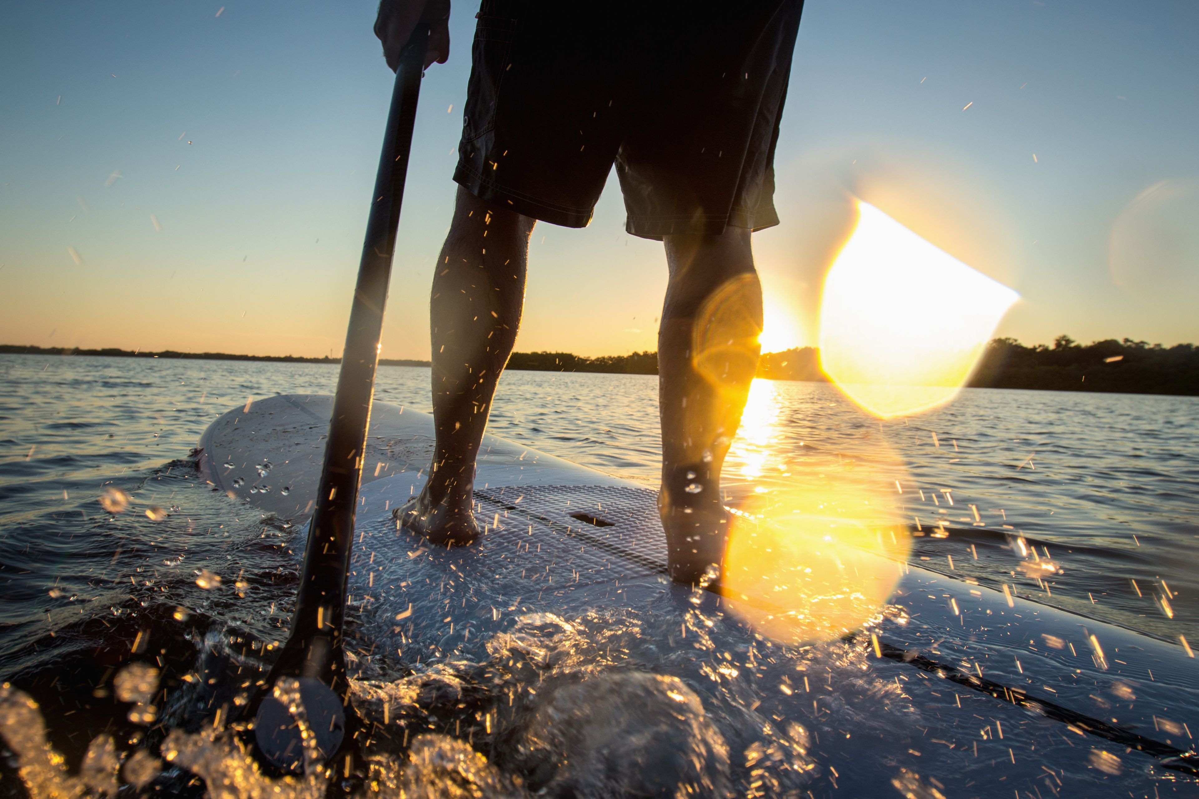 A person standing on a paddleboard in a body of water with the sun setting in the background.