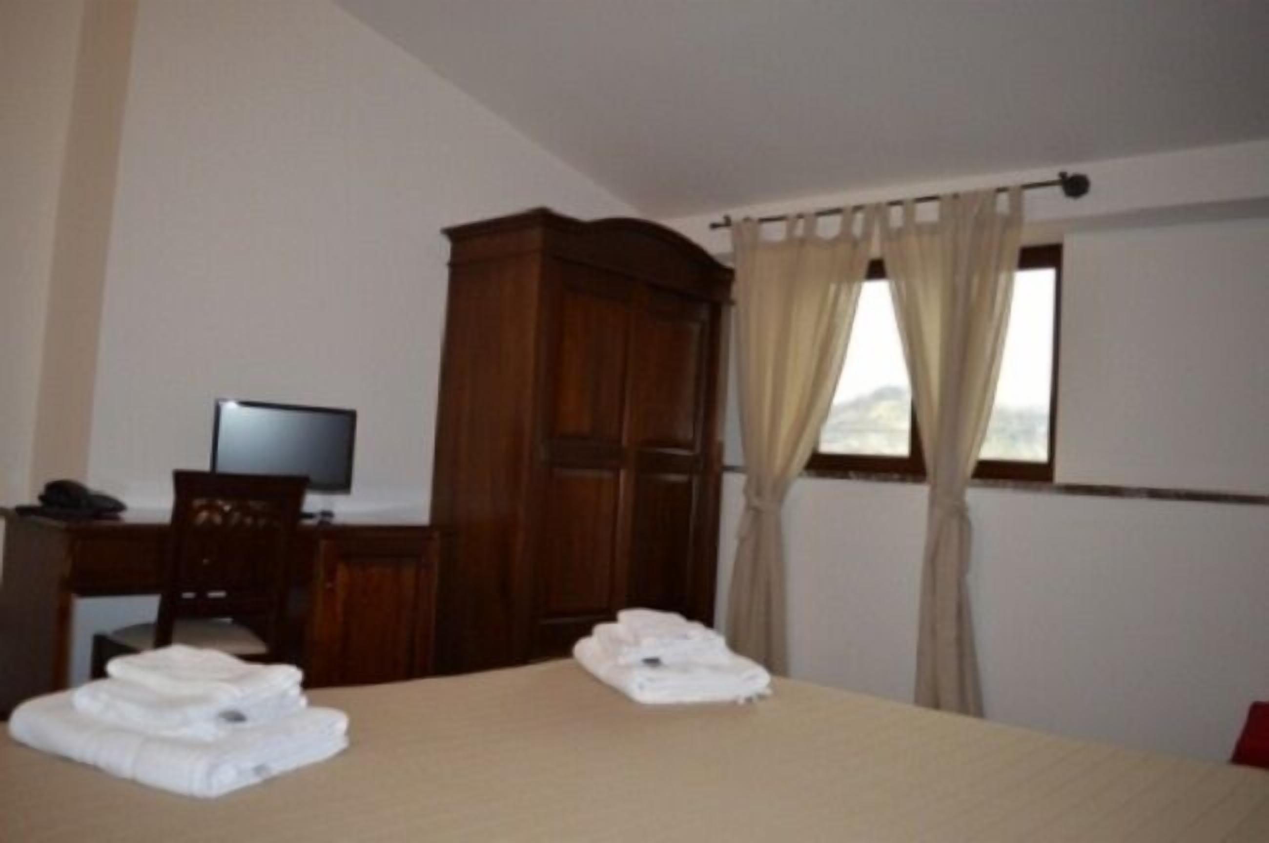 A hotel room with a bed, a desk with a computer, a wardrobe, and a window with curtains.