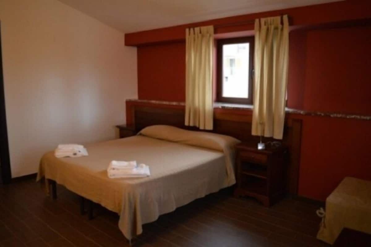 A hotel room with a single bed, a bedside table, and a window with curtains.