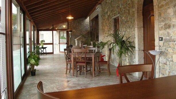 A spacious indoor area with a stone wall, wooden ceiling, and large windows. There are tables and chairs arranged for dining or meetings. - Il Canalotto (Longi)