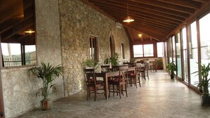 A spacious indoor area with stone walls, wooden tables, and chairs, and large windows allowing natural light. - Il Canalotto (Longi)