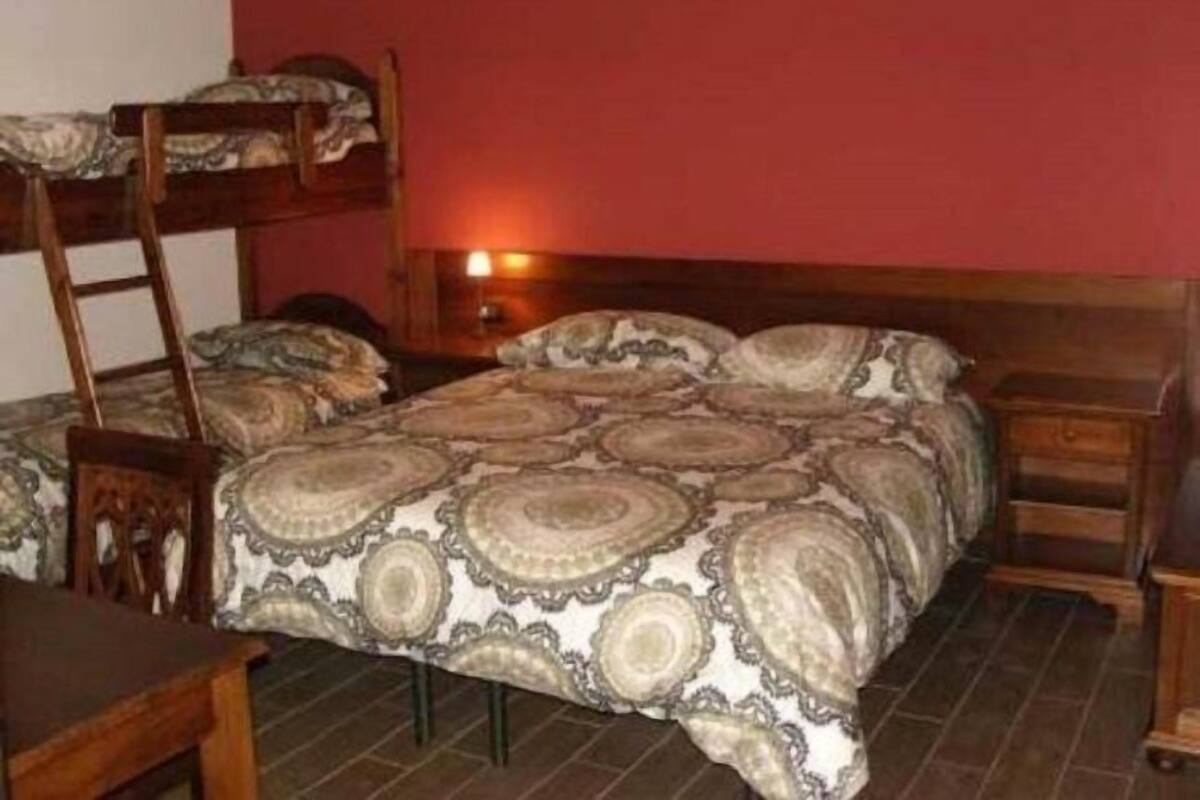A room with a bunk bed, a wooden desk, a chair, and a bedside table with a lamp.