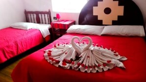 Ein Hotelzimmer mit zwei Betten, eines mit roter Bettdecke und das andere mit weißer Bettdecke. Auf dem Bett mit der roten Bettdecke ist eine Handtuchgestaltung in Herzform zu sehen.