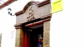 Ein Gebäudeeingang mit roter Tür, steinernen Säulen und einem gelben Schild an der Wand.