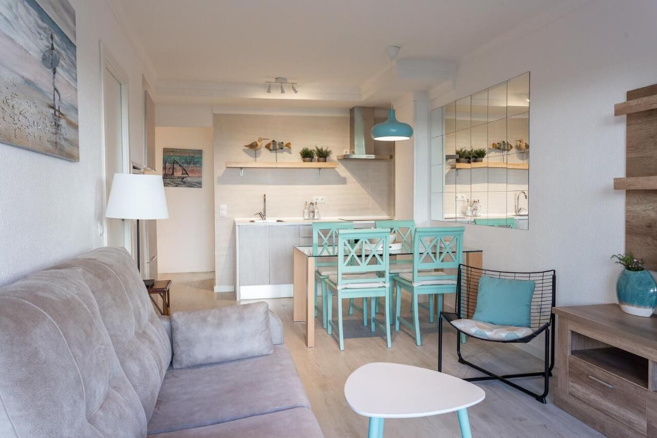 A modern living room with a sofa, a small table, and a dining area with chairs.