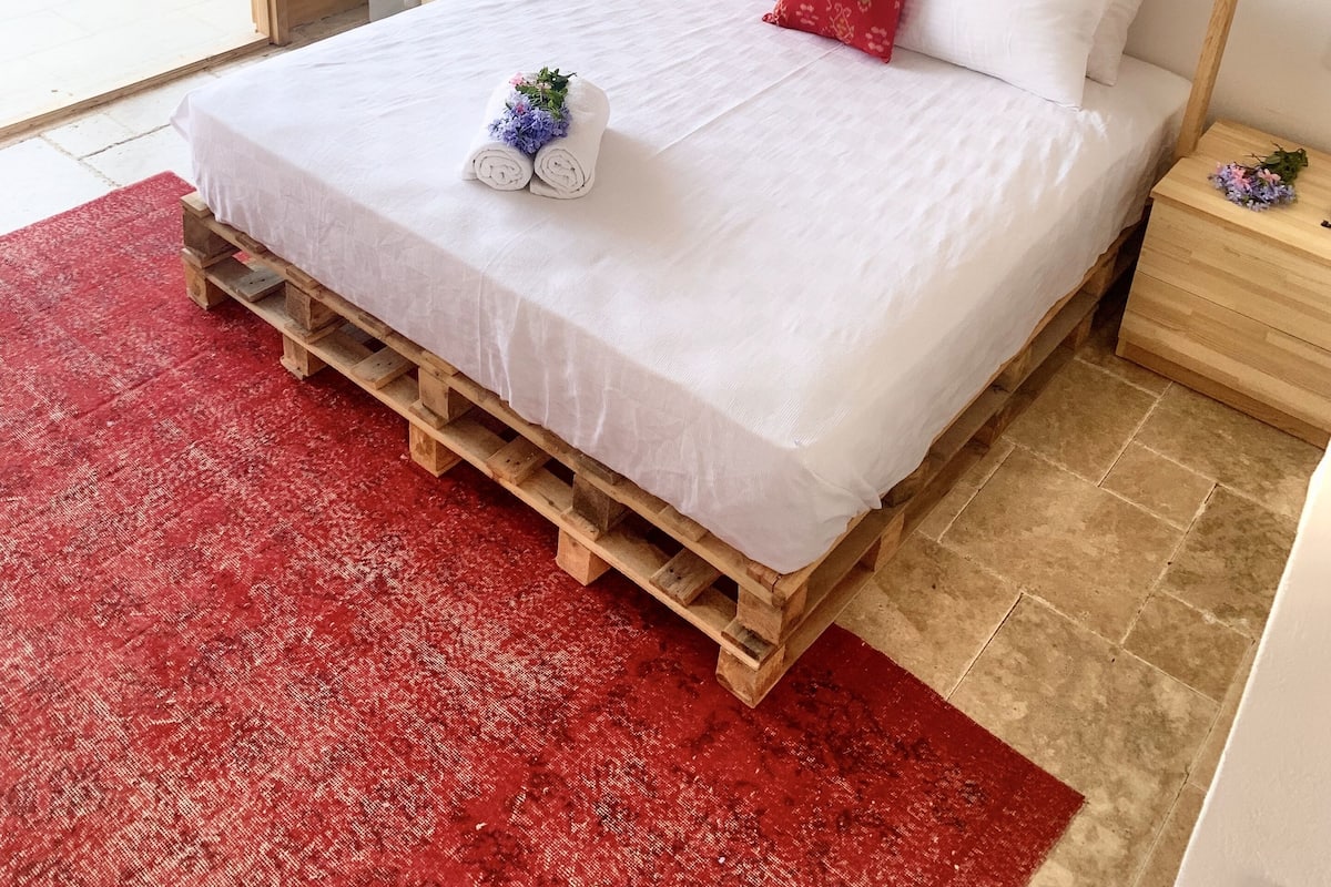 A bedroom with a bed, a round mirror, a bedside table, and a red rug.