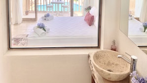 A bedroom with a large window, a bed with towels and flowers, a wooden table and chairs outside, and a stone sink. - Alacati Barbarossa Hotel (Cesme)
