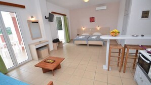 A compact hotel room with a bed, a small kitchenette, a dining area, and a sliding glass door leading to an outdoor area. - Paradiso Aparthotel (Corfu)