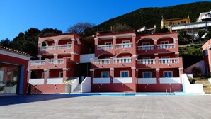 A red building with multiple balconies and a pool area. - Paradiso Aparthotel (Corfu)