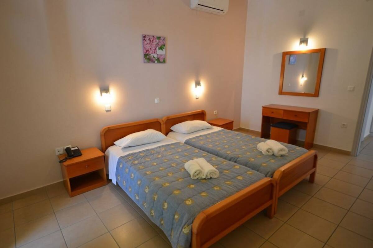 A double bed with a floral bedspread, bedside tables with lamps, a small wooden dresser, and a wall-mounted mirror.