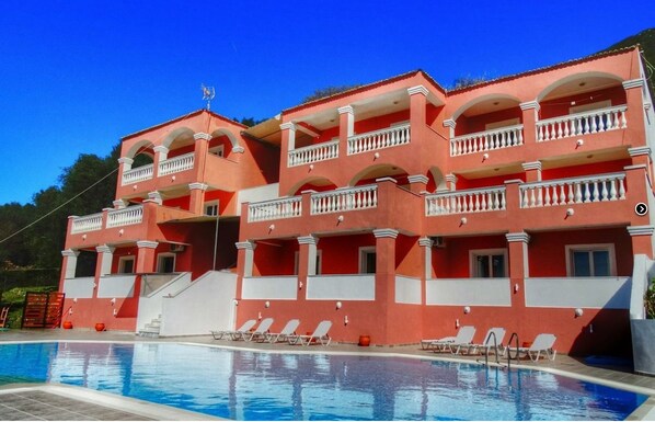 Un hôtel à plusieurs étages doté de balcons, d’une piscine et de chaises longues.