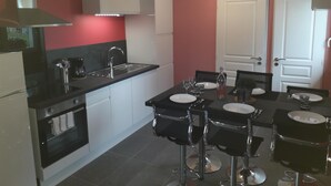 A modern kitchen with a dining area, featuring a black countertop, white cabinets, and a red accent wall.