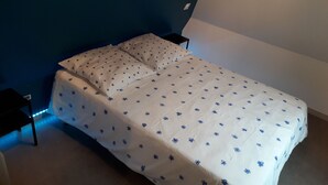 A single bed with a white bedspread featuring blue floral patterns, positioned against a blue wall with a white section to the right.