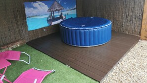 A hot tub with a blue cover, a wooden deck, and a mural of a tropical beach scene.