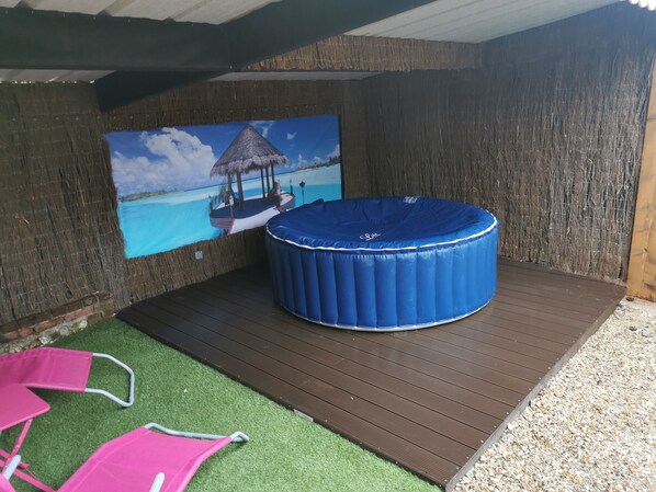 Un jacuzzi con tapa azul, un muelle de madera y un mural de una playa tropical.
