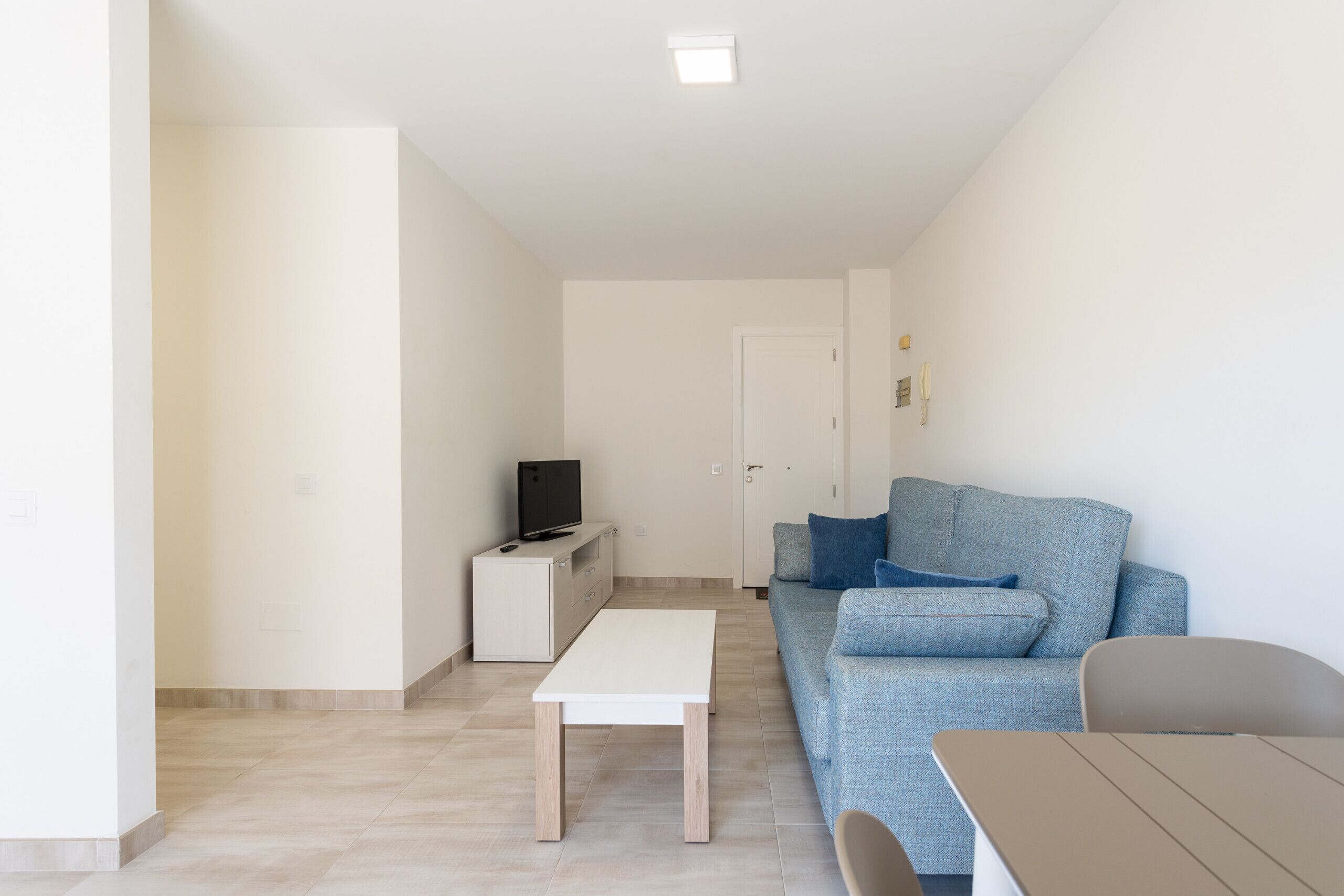A modern living room with a grey sofa, a small white table, and a TV on a cabinet.