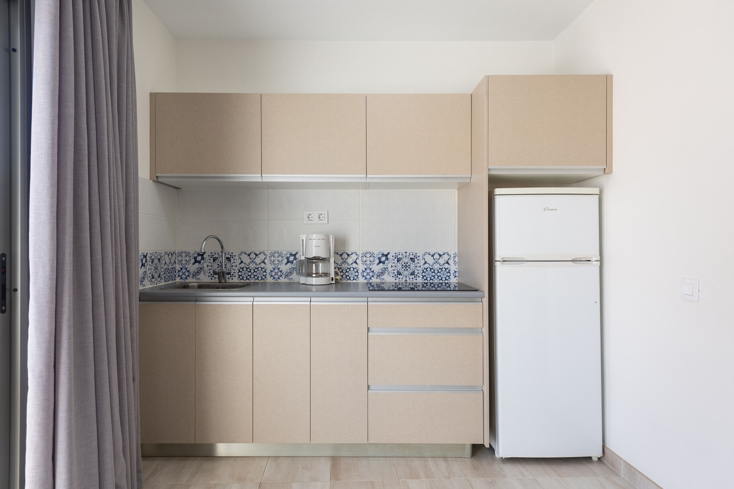 A compact kitchen with beige cabinets, a white refrigerator, and a coffee maker on the countertop.