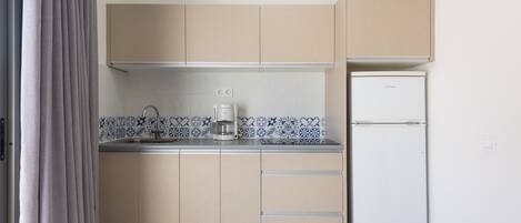 A compact kitchen with beige cabinets, a white refrigerator, and a coffee maker on the countertop.