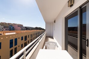 Un balcon avec une chaise blanche, une table et une vue sur les immeubles.