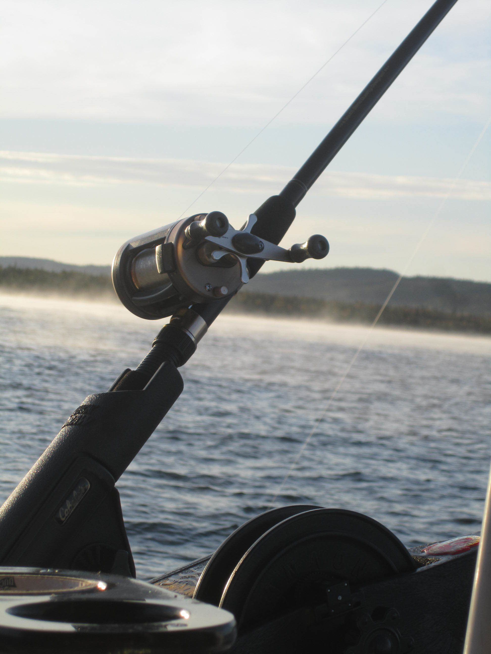 A fishing rod with a reel, a boat wheel, and a calm body of water in the background.