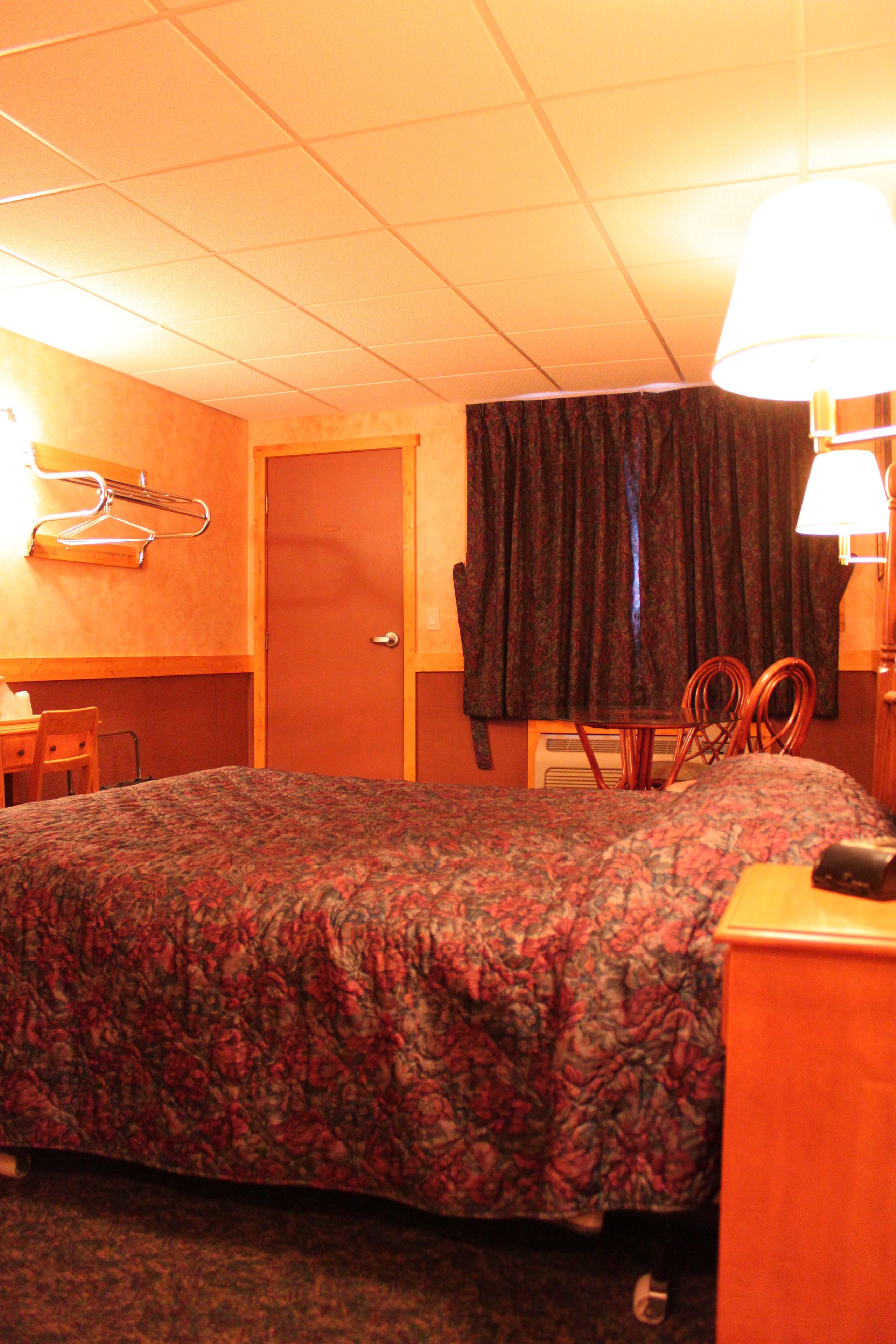 A hotel room with a bed, a chair, a desk, and a lamp.