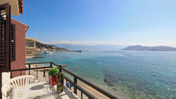 Ein Balkon mit freiem Blick auf ein ruhiges Meer, eine entfernte Küste und ein Gebirge.
