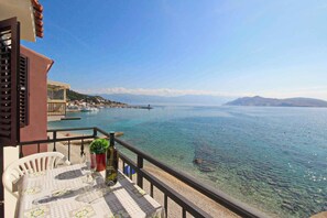 Un balcone con vista libera su un mare calmo, una costa lontana e una catena montuosa.