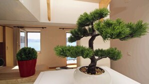 Ein Zimmer mit großem Fenster, einer Bonsai-Pflanze im Topf und einem weißen Tisch.