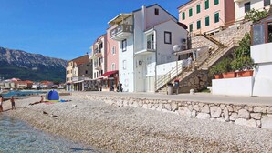 Ein Kiesstrand mit Gebäuden, einer Treppe und einem Berg im Hintergrund.
