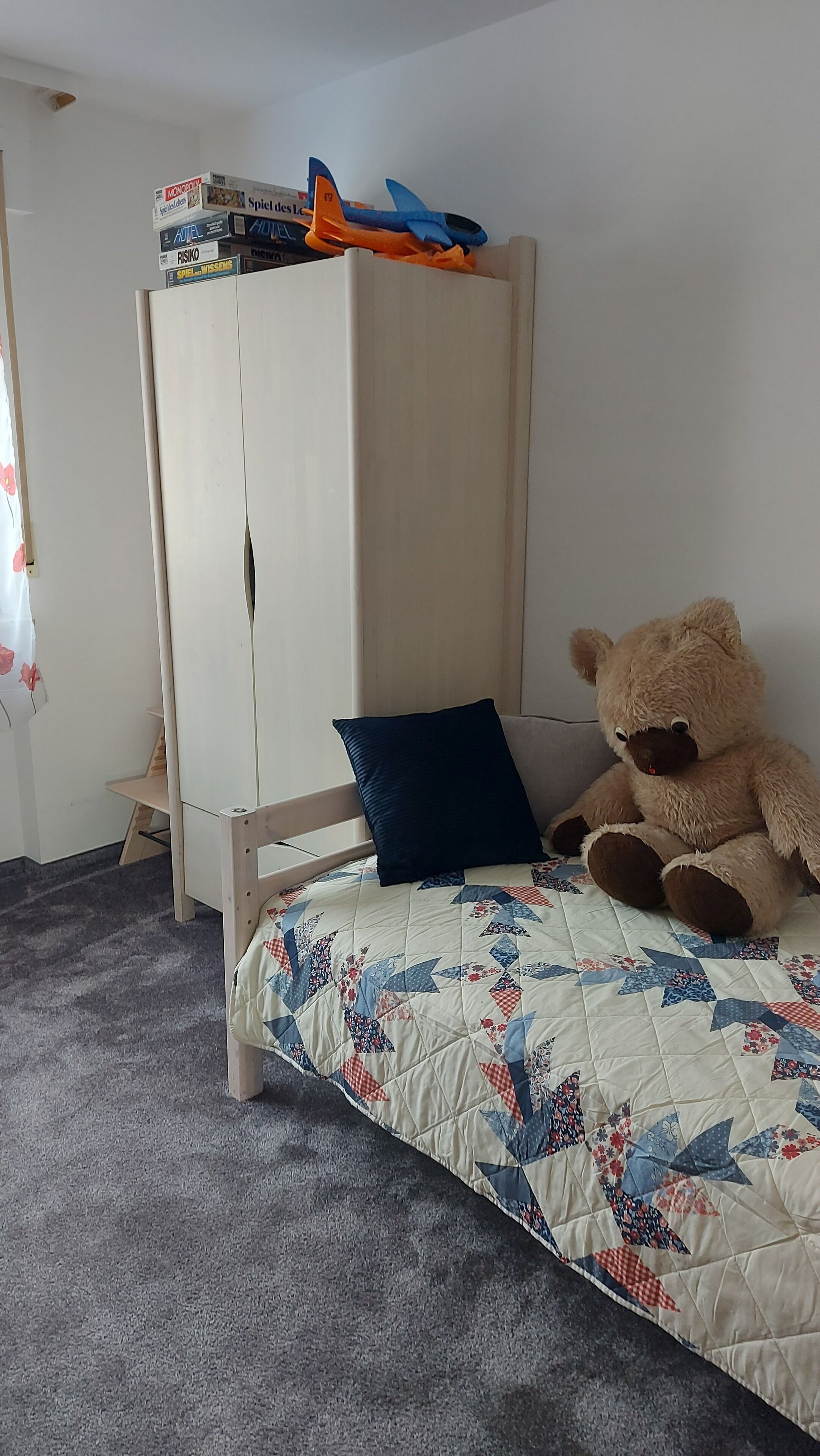 Ein Schlafzimmer mit einem Bett, einem Teddybären, einem Kleiderschrank und einem kleinen Tisch.