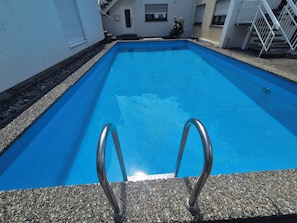 Ein rechteckiger Pool mit glasklarer, blauer Wasseroberfläche, umgeben von einem Beckenrand aus Kies.