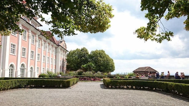 En velanlagt formel have med symmetrisk anlæg, en stor bygning med rosa og hvid facade, samt en pavillon i baggrunden.