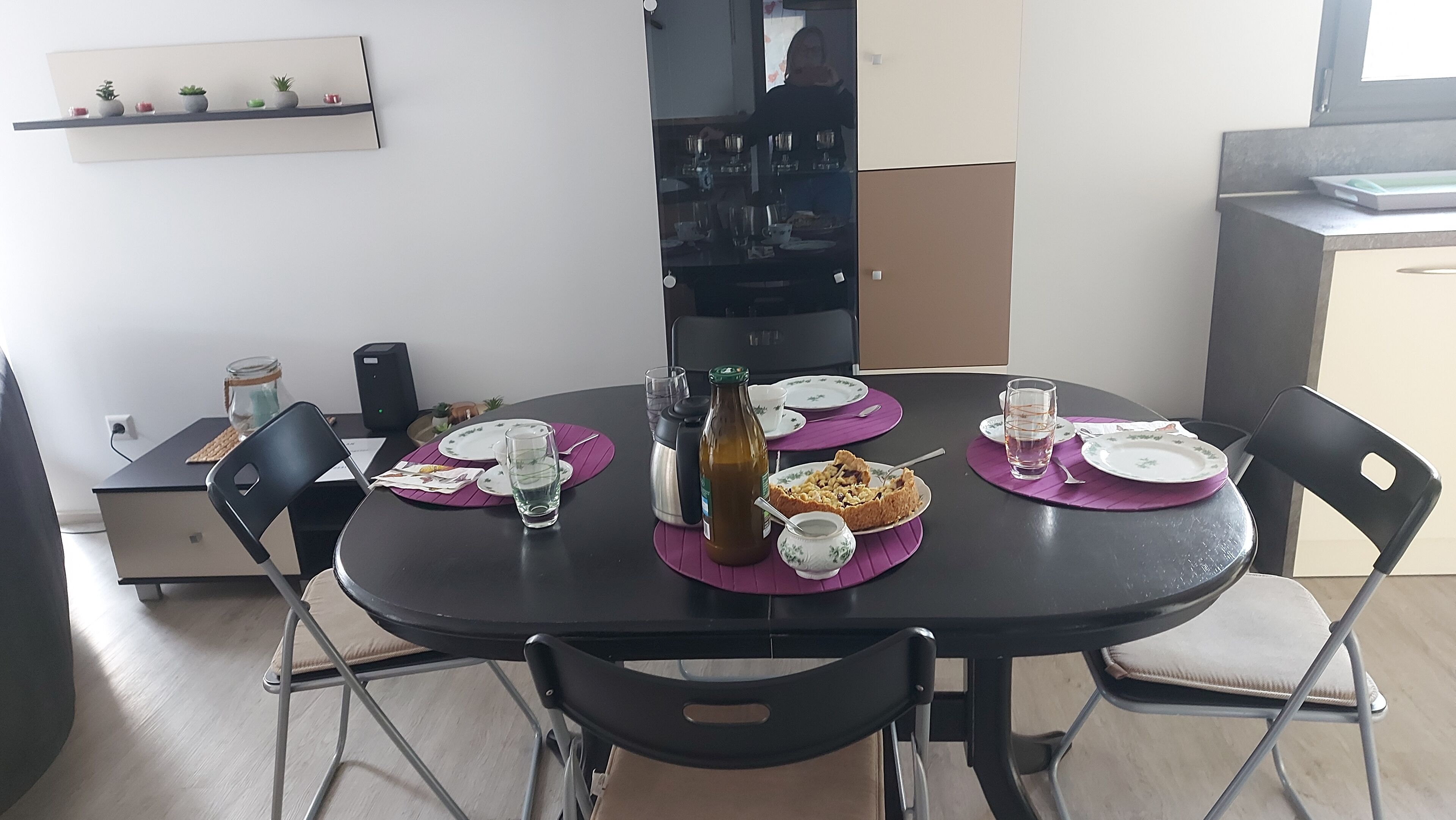 A dining table with purple placemats, plates, and cutlery. There are chairs around the table, a bottle, and a glass on the table.