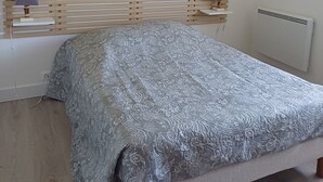 A bedroom with a wooden slat headboard, a grey patterned bedspread, and three wall-mounted floral paintings. - APARTMENT IN HOUSE (Lacapelle-Viescamp)